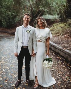 a man and woman standing next to each other in front of trees with leaves on the ground