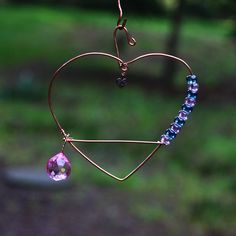 a heart shaped wind chime hanging from a wire with a beaded necklace attached to it