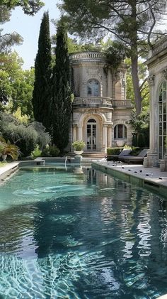 an outdoor swimming pool in front of a large house with trees and bushes around it