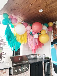 balloons and streamers are hanging from the ceiling above an outdoor kitchen area with a bbq