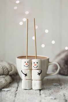 two marshmallows with faces drawn on them in front of a cup filled with hot chocolate