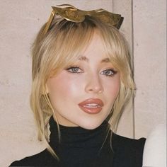 a woman with blonde hair wearing a black turtle neck top and gold bow tie around her head