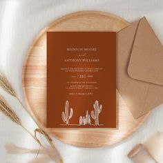 an orange wedding card on top of a wooden plate next to some brown envelopes