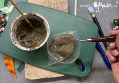 a person is holding a paintbrush and painting the inside of a bowl on a green tray