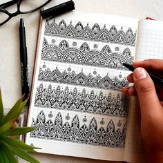 a person holding a pen and writing on a notebook with an intricate pattern in it