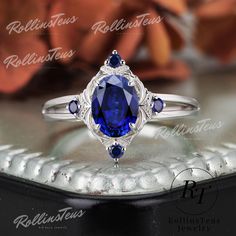 an oval shaped blue sapphire and diamond ring sits on top of a silver tray with flowers in the background