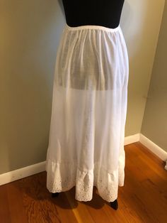 1970s long white cotton blend half slip with eyelet flounce: This lovely 1970s maxi half slip has an elasticized waistline. It ends with a wide eyelet flounce. It was made by Fritzi. Measurements: Waist 20-34 in. elasticized. Hips full Length 32 in. White Petticoat For Daywear In Spring, White Petticoat For Summer Daywear, Summer White Petticoat For Daywear, White Spring Petticoat For Daywear, White Non-slip Summer Slip-ons, Slip-resistant White Sole Slip-ons, 1970s Style Full-length Cotton Bottoms, White V-neck Spring Nightgown, Full Slip Vintage