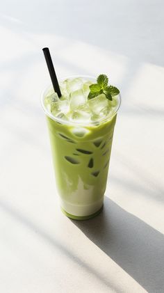 a green drink with ice and mint garnish on the rim, sitting on a white surface