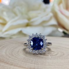 a blue and white ring sitting on top of a piece of wood with flowers in the background