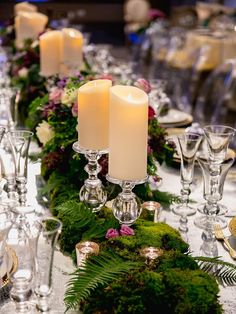 a long table with candles and greenery on the top, surrounded by wine glasses