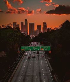 the sun is setting over a highway with cars on it and tall buildings in the background