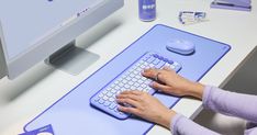 a woman is typing on a blue computer keyboard and mouse pad at a desk with various office supplies around her