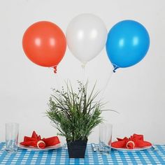 three balloons are floating over a table with plates and glasses on it, along with a potted plant