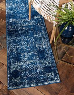 a blue area rug on a wooden floor with a chair and potted plant in the background