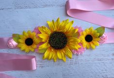 two sunflowers and pink ribbon on a white wooden surface with ribbons around them