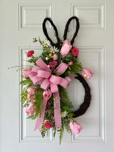 a wreath with pink flowers and bunny ears hanging on a door