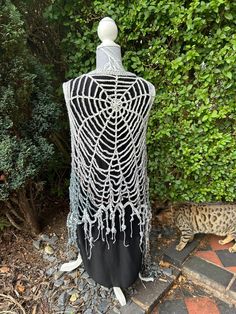 a black and white dress with fringes on it sitting in front of some bushes