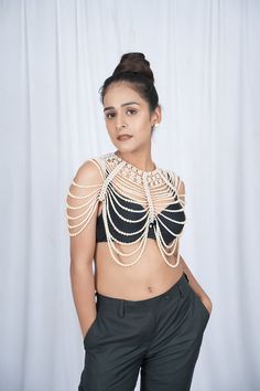 a woman in black pants and a crop top with pearls on her chest is posing for the camera