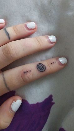 a woman's hand with some small tattoos on her thumb and ring, while the other finger has a spiral design