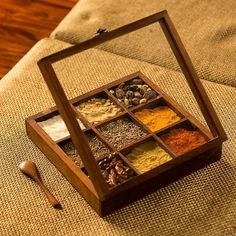 an open wooden box filled with spices on top of a couch next to a spoon