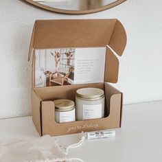 an open box containing two candles and a note card on a white table with a mirror in the background