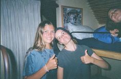 two girls giving the thumbs up while standing in front of a bunk bed with other people