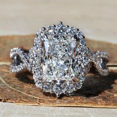 an oval cut diamond surrounded by smaller round diamonds sits on top of a piece of wood