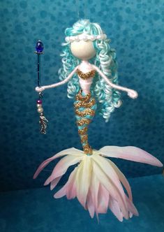 a doll with blue hair is standing on a pink flower and holding a wand in her hand