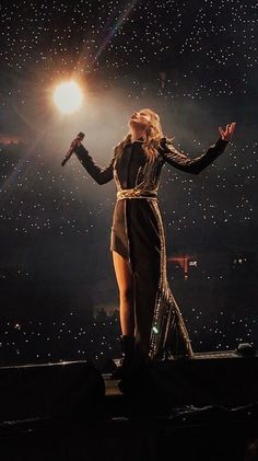 a woman standing on top of a stage in front of a microphone with her arms outstretched