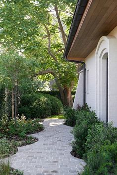 a brick walkway leading to a white house with trees and shrubbery on either side