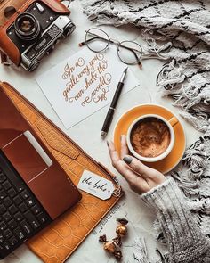 a woman holding a cup of coffee next to a laptop computer and other personal items