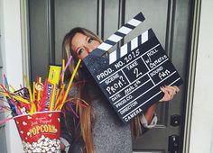 a woman holding a clapper and popcorn bucket in front of her face while standing next to a door