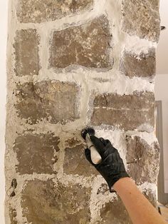 a person in black gloves painting a brick wall with white and brown paint on it