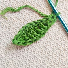 a crochet hook with a green leaf on it next to a knitting needle