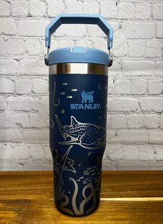 a blue insulated cup sitting on top of a wooden table next to a brick wall