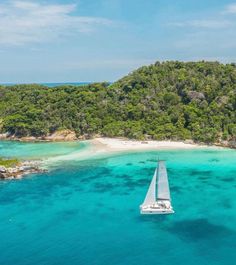 an aerial view of a sailboat in the water near a sandy beach and forested area