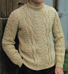 a man wearing a sweater and hat standing next to a wooden fence