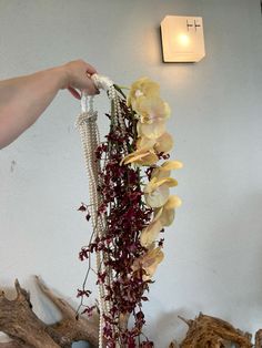 a vase with flowers and pearls hanging from it's side in front of a wall