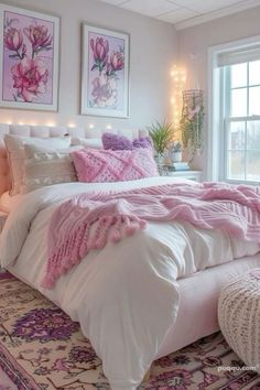 a white bed with pink comforter and pillows in front of a large window filled with flowers