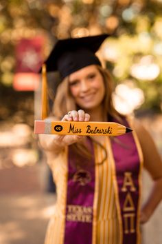 a woman in a graduation gown holding up a pencil with the words miss berenski written on it