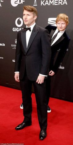 two men in tuxedos standing on a red carpet