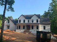 a large white house sitting in the middle of a forest next to a pile of dirt