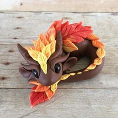 a brown dragon figurine with leaves on it's head sitting on a wooden surface