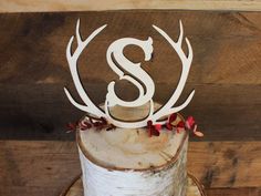 a white cake with antlers and the letter s on top is sitting on a wooden stand