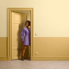 a woman standing in an open doorway with her back to the camera, wearing a purple dress and green boots