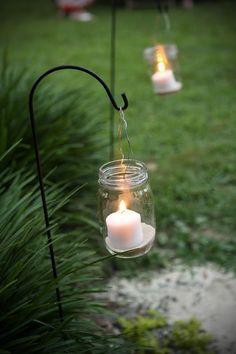 three lit candles hanging from a wire in a field with grass and water behind them