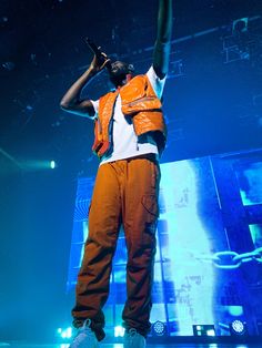 a man in an orange vest and white shirt on stage with his arms raised up