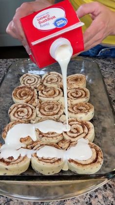 cinnamon rolls being drizzled with icing from a red box on a baking sheet