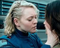 two women are talking to each other in front of a bus and one has her eyes closed