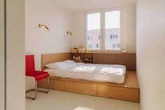 a bed sitting under a window in a bedroom next to a desk with a red chair